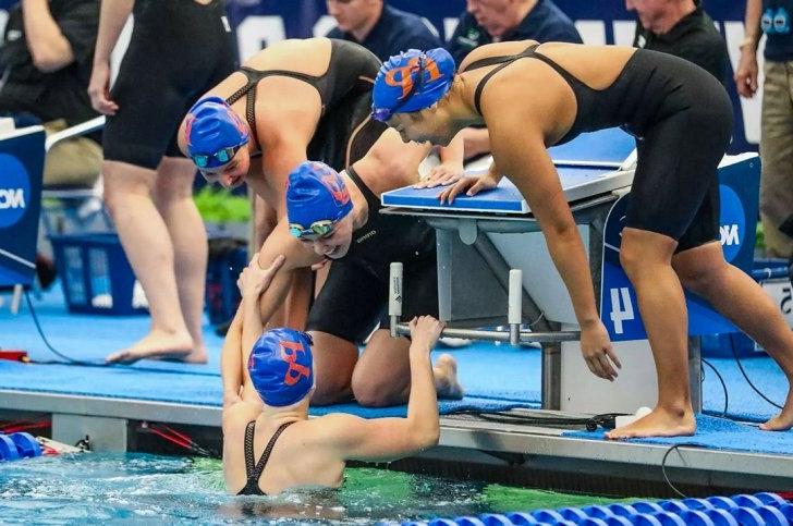 Four members of the Pomona-Pitzer women's swim and dive team enthusiastically greet each other at the pool.